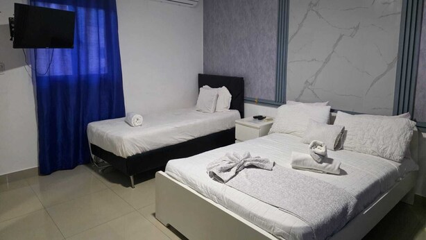 Habitación de hotel con dos camas, un televisor de pantalla plana, un equipo de aire acondicionado y una ventana con diseño de pared tipo mármol.