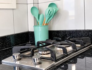 A kitchen with a gas stove, a teal utensil holder, and a black countertop. - Sol Caribe Sleep&Go (Punta Cana)