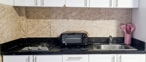 Una cocina con armarios blancos, encimera negra, un tostador, un fregadero y un salpicadero de mármol.