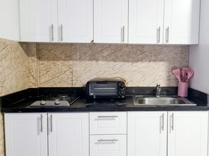 A kitchen with white cabinets, a black countertop, a toaster, a sink, and a marble backsplash. - Sol Caribe Sleep&Go (Punta Cana)