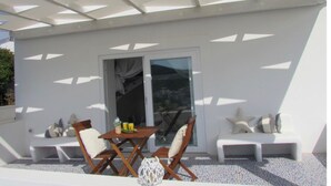 Ein moderner Außenbereich zum Sitzen mit Tisch und Stühlen, einer Glastür und einer weißen Außenwand.