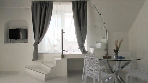 Ein modernes Zimmer mit Treppe, Flachbildfernseher, Esstisch mit Stühlen und einem fenster mit Vorhängen.