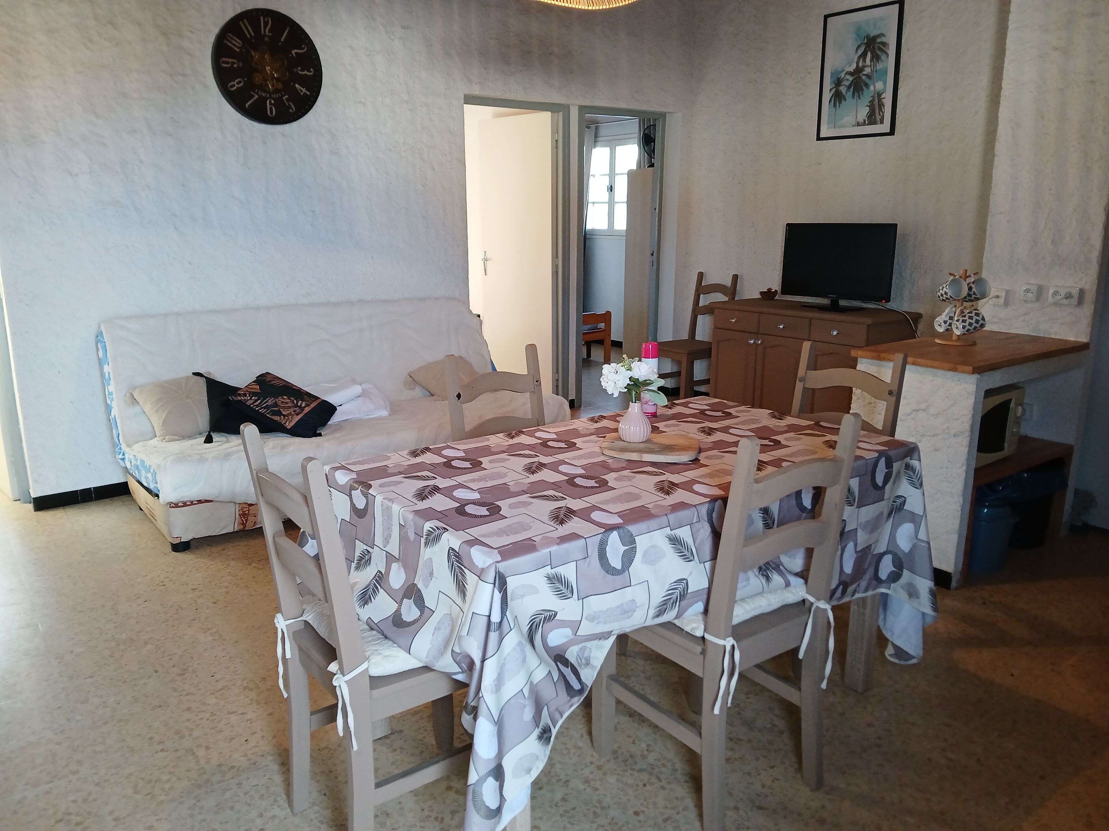 Una sala de estar con un sofá, una mesa de comedor con sillas, un televisor y un reloj en la pared.