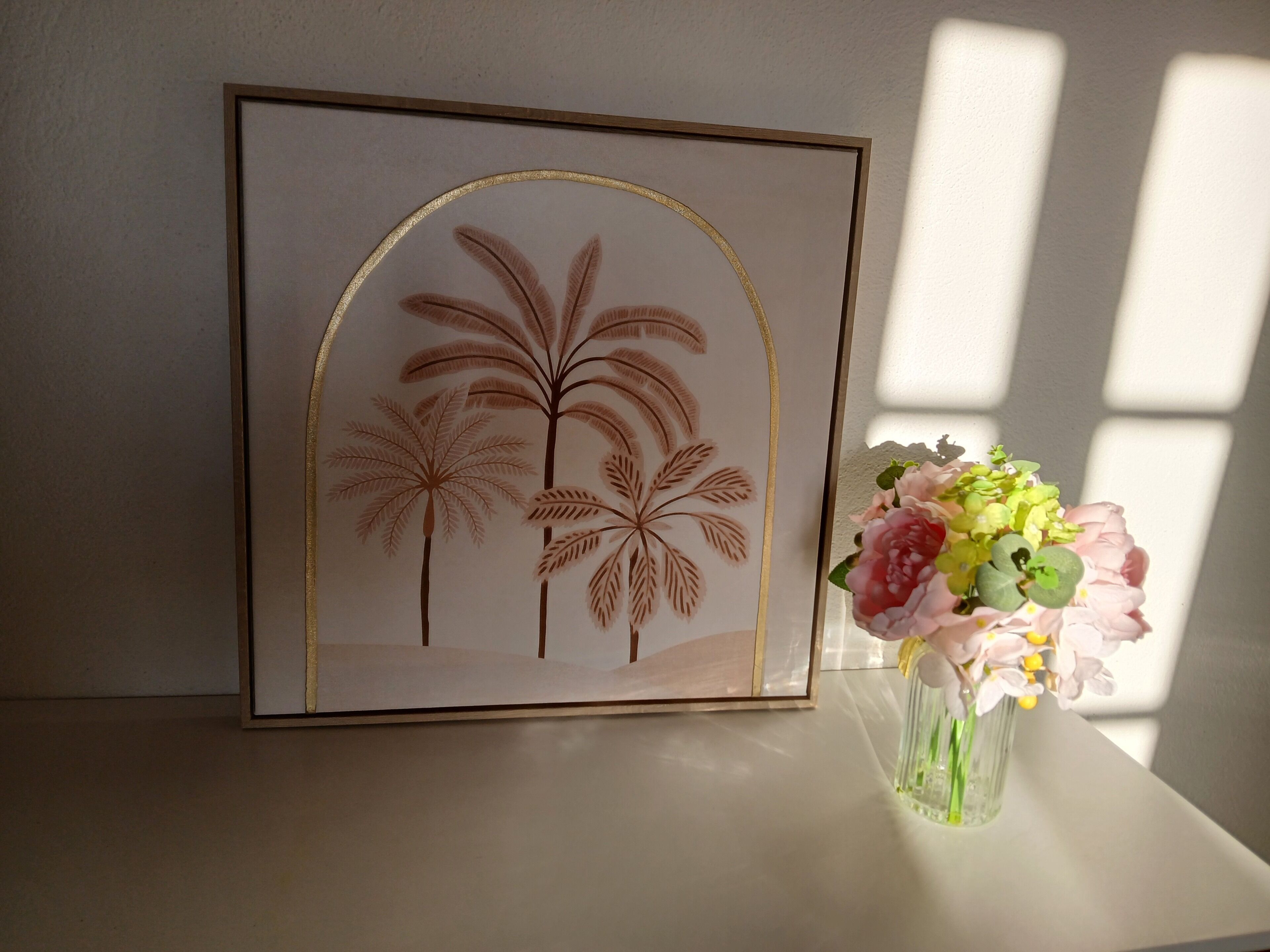 Ein gerahmtes Kunstwerk mit Palmen und einer Blumenvase auf einem Tisch.