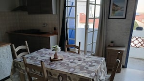 A dining area with a table set for four, a vase with flowers, and a view of the outside. - Lovely apartment 2 steps from the beach and all amenities! (SAINT CYPRIEN)