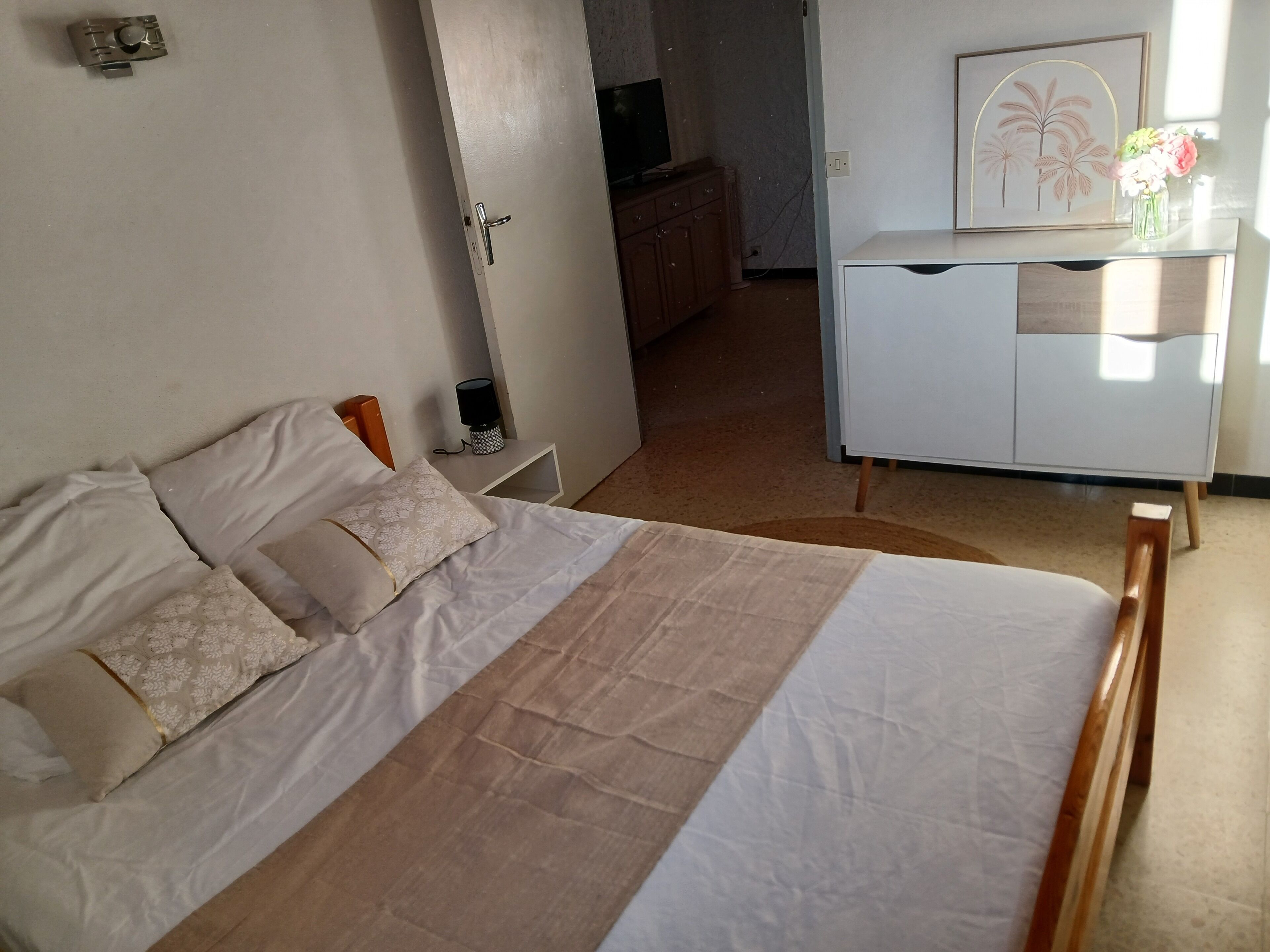 A bedroom with a bed, bedside tables, a dresser, and a wall-mounted TV.
