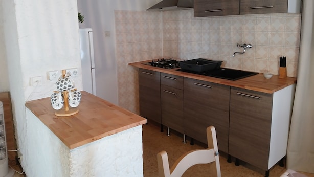 A compact kitchen with a wooden countertop, a gas stove, and a sink. There are cabinets above the countertop and a white chair in the foreground. - Lovely apartment 2 steps from the beach and all amenities! (SAINT CYPRIEN)