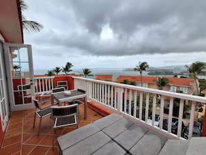 Ein Balkon mit Tisch und Stühlen mit Blick auf eine Küstenlandschaft, Palmen und Gebäude.