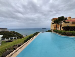 A swimming pool with a view of the ocean, a building with a red roof, and a well-maintained lawn. - 2 Bedrooms 2 Baths 3 Pools Villa in Fajardo (Fajardo)