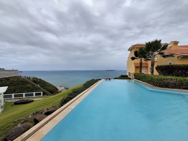 Ein Swimmingpool mit Blick auf den Ozean, ein Gebäude mit rotem Dach und ein gepflegter Rasen.