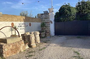 Señalización para 'Le Dimore Wine & Resort', con un muro de piedra, un portón y jardinería.