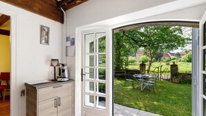 A room with a kitchen counter, a coffee maker, a dining table with chairs, and a view of a garden through a glass door. - Rural Cottage “La Rivière Assoiffée” with Garden and Wi-Fi (Florimont-Gaumier)