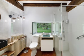 A bathroom with a toilet, sink, and shower. There is a window with a view of greenery outside.