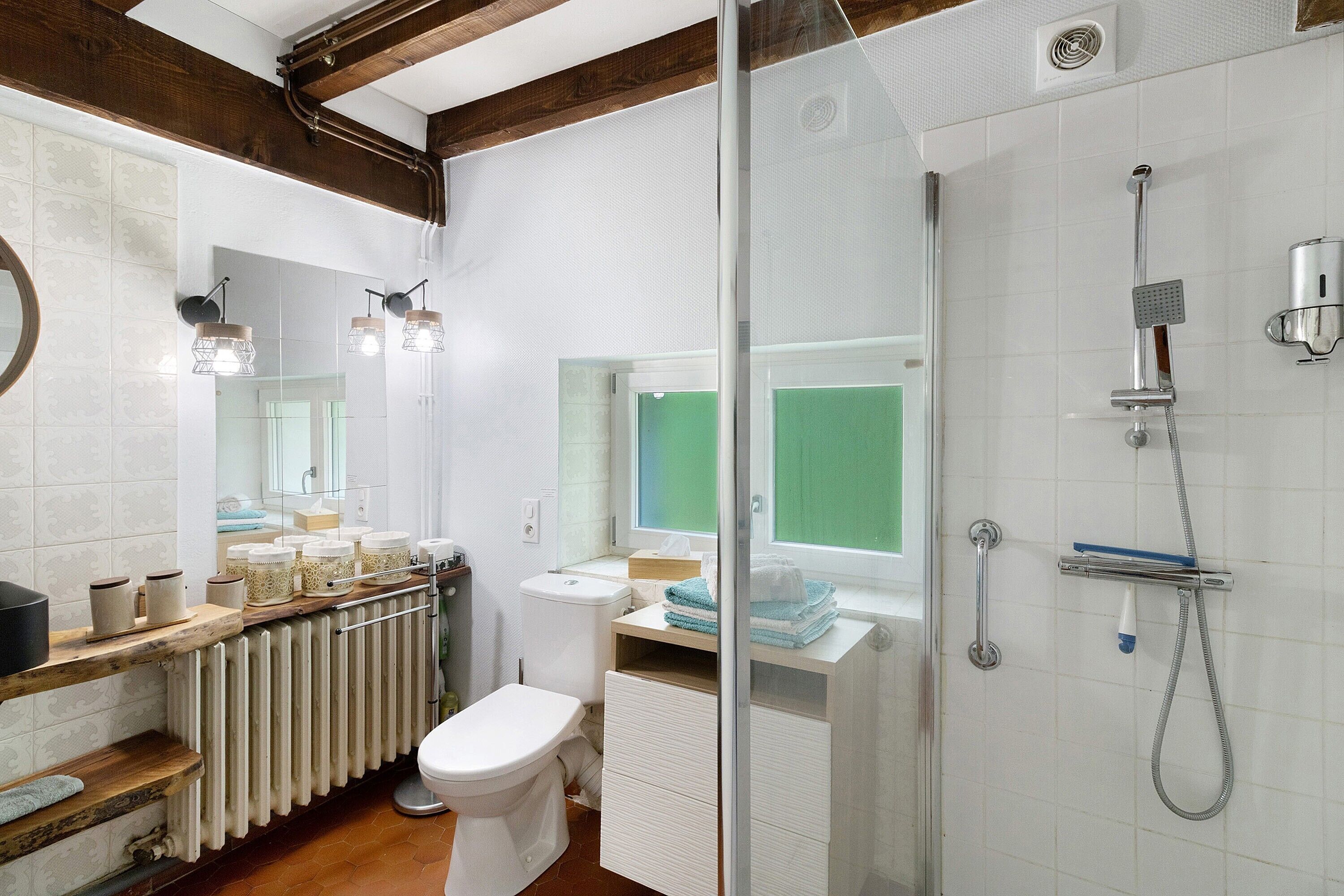 Un baño con inodoro, lavamanos, ducha y cabina de ducha con mampara de vidrio.