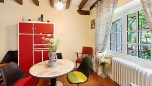 A dining area with a red cabinet, a table with chairs, a hanging light fixture, and a window with curtains. - Rural Cottage “La Rivière Assoiffée” with Garden and Wi-Fi (Florimont-Gaumier)