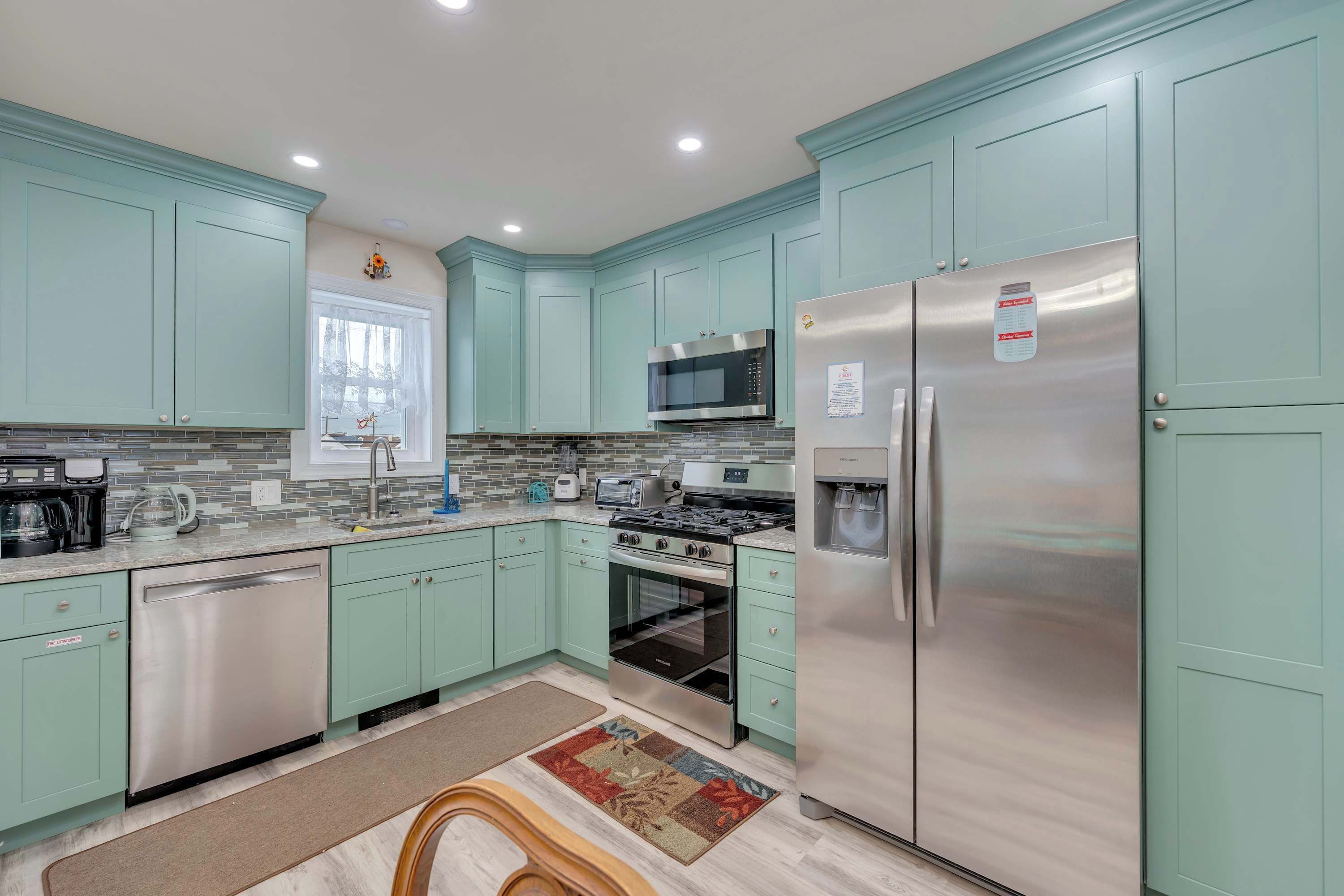 A kitchen with teal cabinets, stainless steel appliances, a microwave, a refrigerator, and a window.