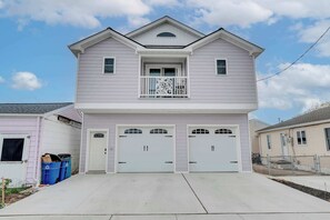 A two-story house with a balcony, two garage doors, and a small porch area. - Sunny Crest Stay – NEW 2BR, Near Beach (Wildwood)