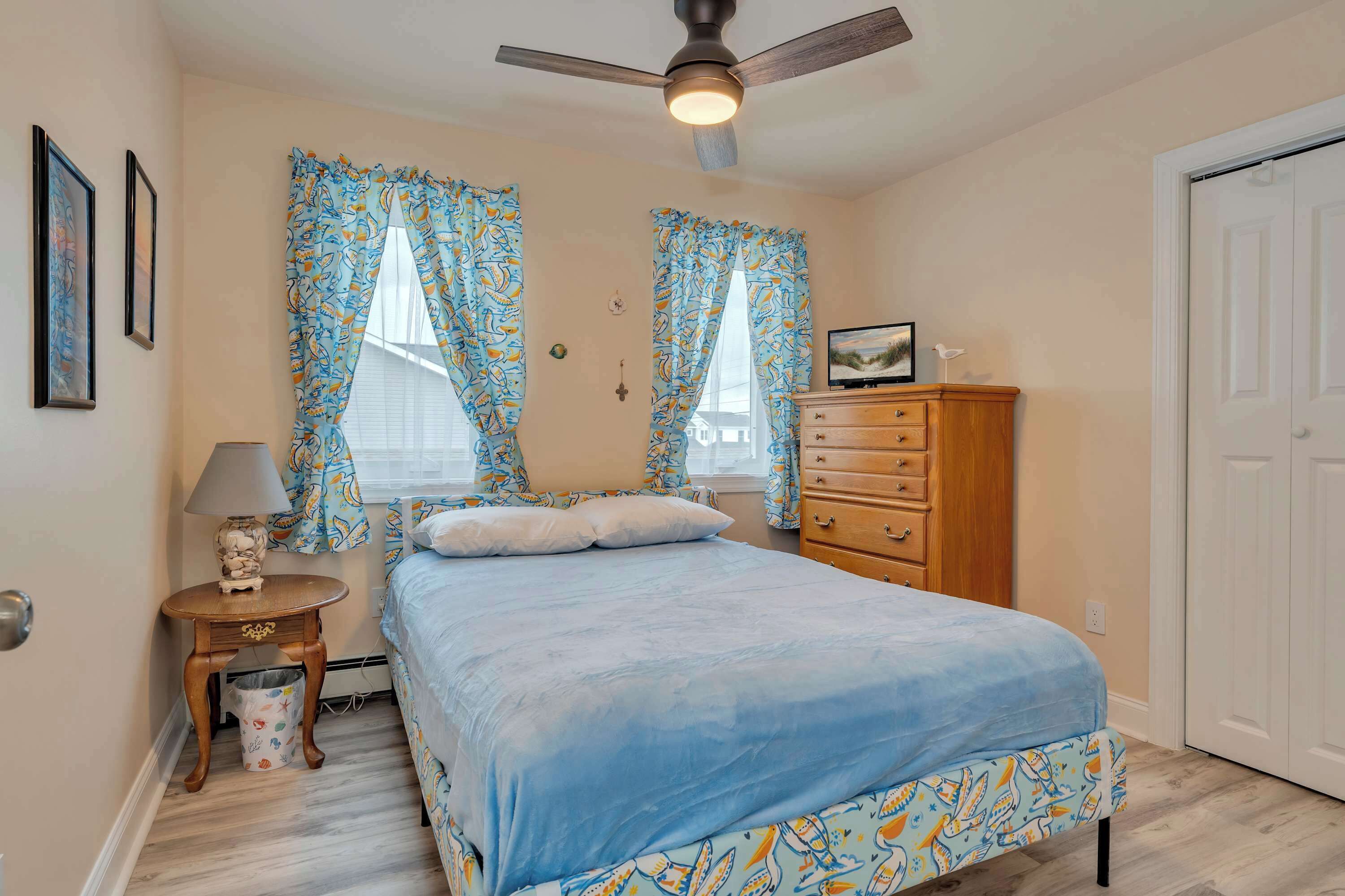 A bedroom with a bed, a dresser, a nightstand, a ceiling fan, and curtains.