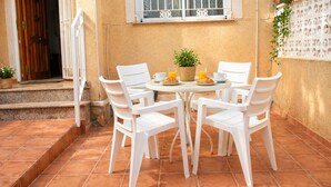Eine Terrasse mit einem runden Tisch und weißen Stühlen, einem kleinen Blumentopf sowie einem Korb mit einem Croissant und Orangensaft.