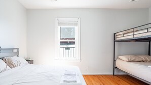 Ein Schlafzimmer mit Etagenbett, einem Einzelbett, einem Fenster mit Jalousien und Holzboden.