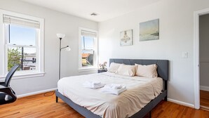 Ein Schlafzimmer mit einem Bett, zwei Fenstern, einer Stehlampe und Bildern an der Wand.