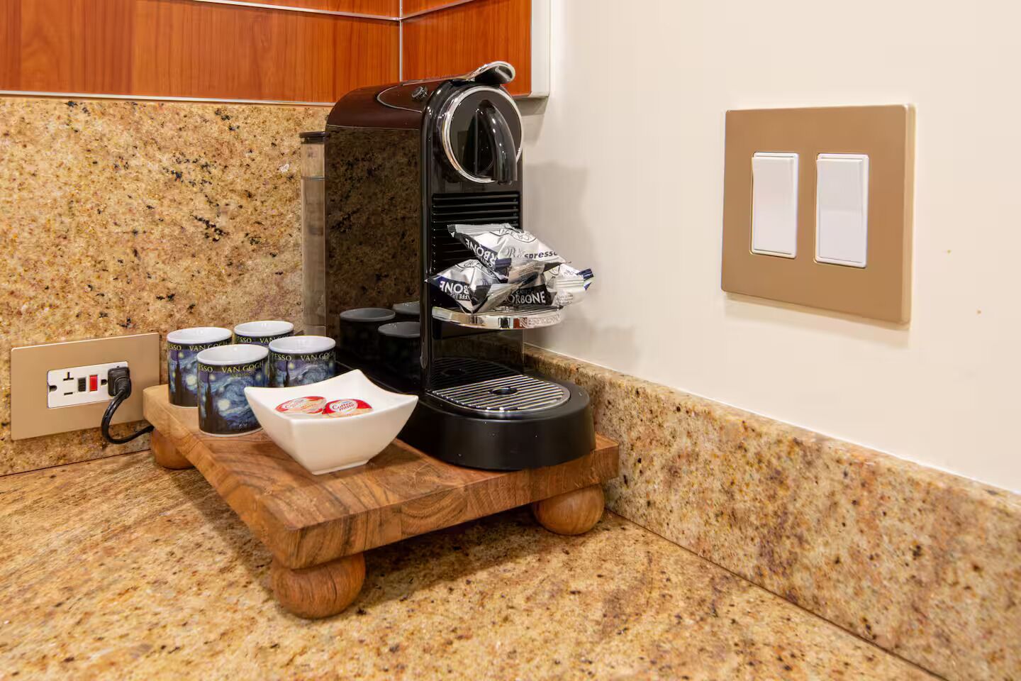 A coffee station with a coffee machine, a bowl of coffee pods, and several coffee cups on a wooden stand.