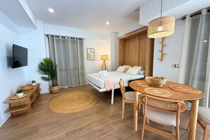 A modern room with a bed, a dining table with chairs, a TV mounted on the wall, and a large window with curtains. - Mediterranean Apartment 6F WIFI+AACC (Valencia)
