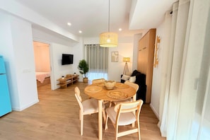 A modern living room with a dining area, wooden flooring, a television, and a large window with curtains. - Mediterranean Apartment 6F WIFI+AACC (Valencia)