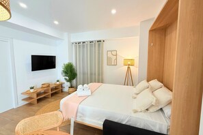 A modern hotel room with a bed, a TV, a desk with a lamp, and a potted plant. - Mediterranean Apartment 6F WIFI+AACC (Valencia)