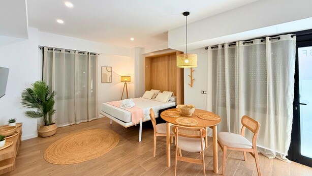 Quarto moderno com cama, mesa de cabeceira, luminária e um espaço de jantar com cadeiras e mesa.