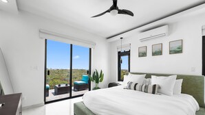 Une chambre moderne avec un grand lit, un ventilateur de plafond et une vue sur un espace de détente extérieur, accessible par une porte-fenêtre coulissante.