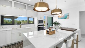 Une cuisine moderne avec des meubles blancs, un grand îlot central et des luminaires suspendus.
