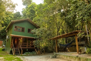 Una casa verde con terraza de madera, rodeada de un bosque denso.