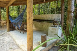 Uma pérgola de madeira com uma rede, uma pia de pedra e um banco.