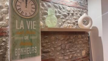 A rustic stone wall, a clock with 'LA VIE DE BONHEURS' text, and a shelf with a vase.