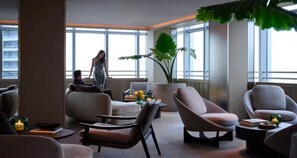 Ein stilvoller Lounge-Bereich mit bequemen Sitzmöglichkeiten, einer großen Pflanze und Blick auf die Stadt.
