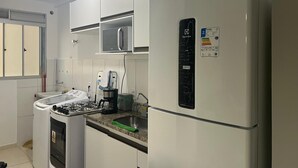 Eine moderne Küche mit weißen Schränken, einer eingebauten Mikrowelle, einem Kühlschrank mit digitaler Anzeige, einem Gasherd und einer Kaffeemaschine.