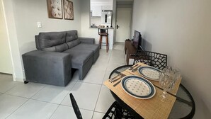 Ein Wohnzimmer mit grauem Sofa, einem Esstisch mit Tellern und Besteck sowie einem Deckenventilator.