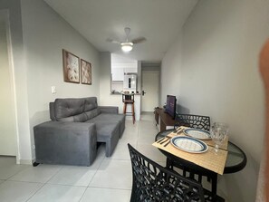 A living room with a grey sofa, a dining table with chairs, a ceiling fan, and a kitchen in the background. - Cozy Apartment in Salvador (Salvador)