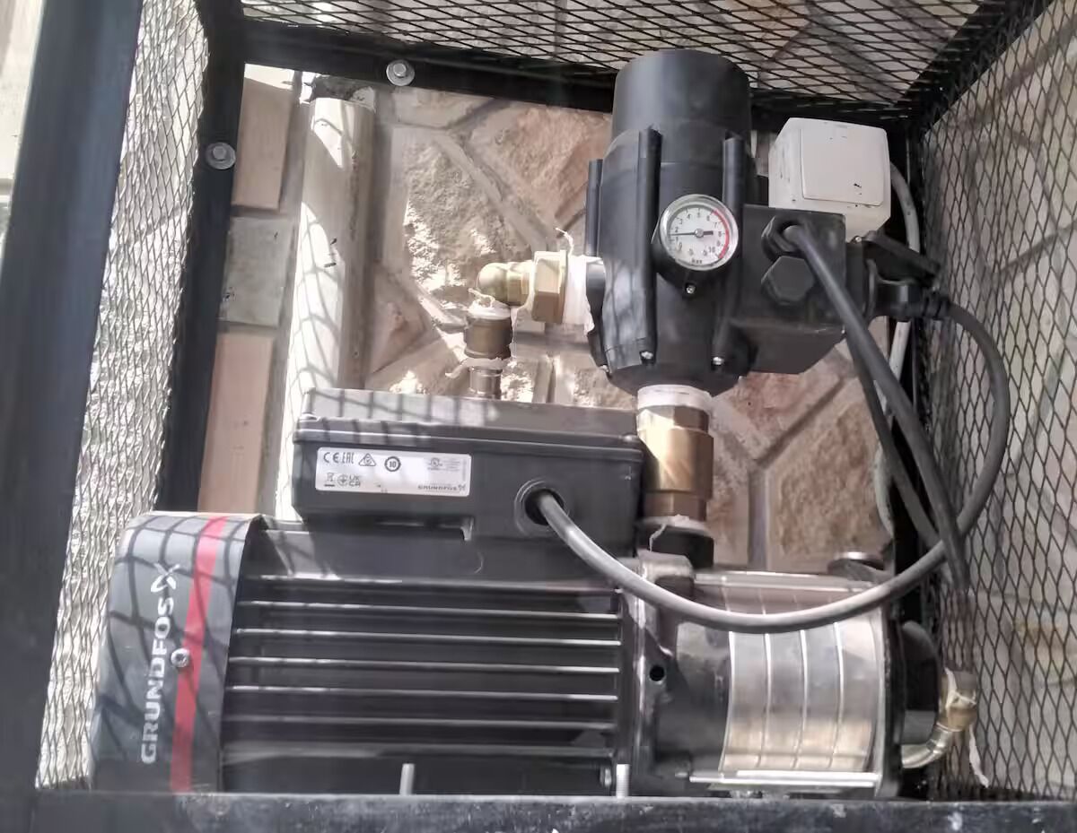A mechanical setup with a pressure gauge, a pump, and a control box, likely part of a water system.