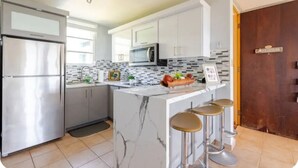 Una cocina moderna con refrigerador, microondas e isla de mármol con taburetes.
