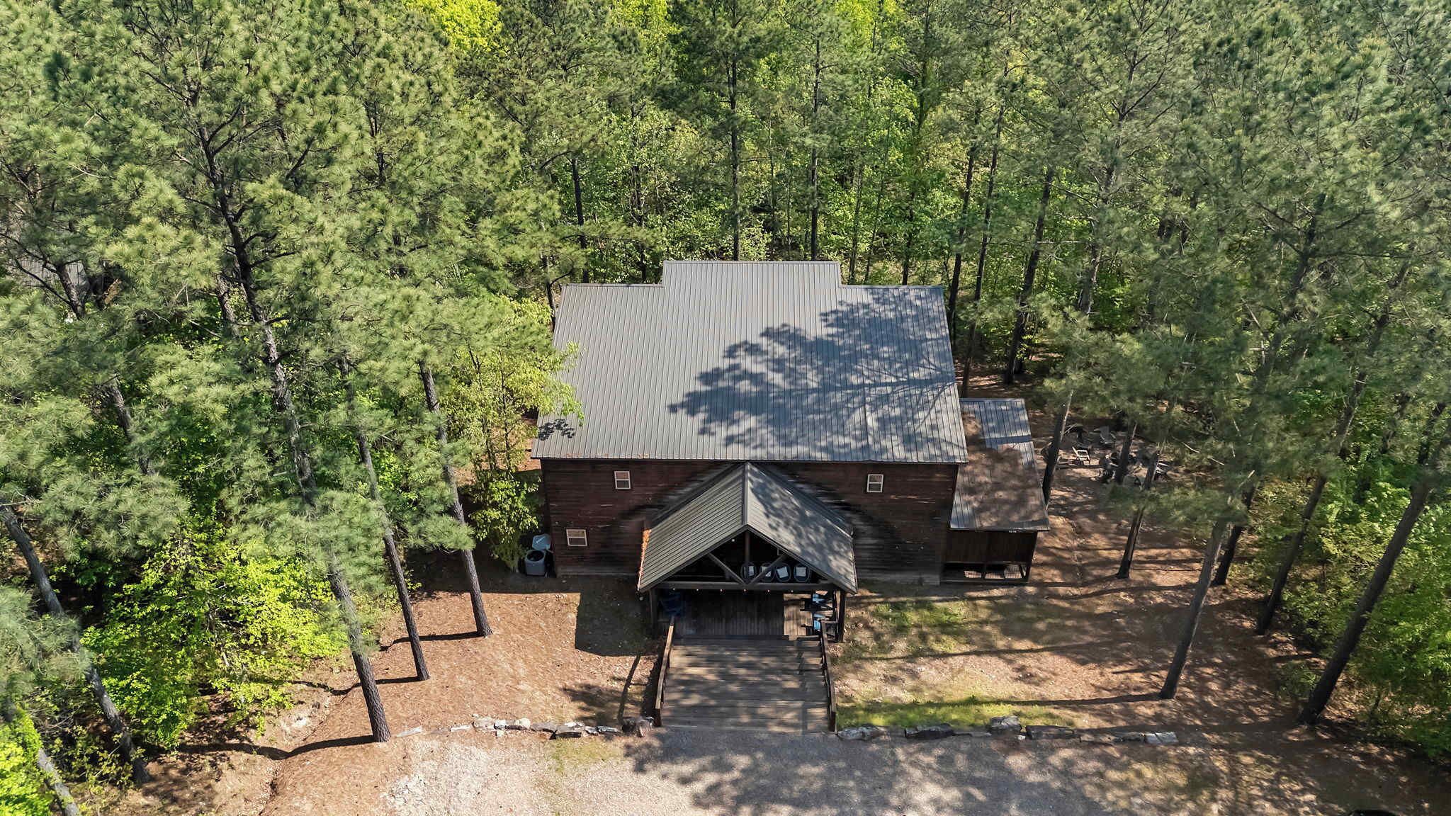 A cabin surrounded by dense forest, with a metal roof and a front porch.