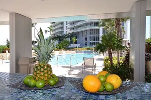 A poolside area with a tropical fruit display, a lounge chair, and a view of a multi-story building. - ★@ EXCLUSIVE Large Luxury Water View FREE Parking★ (Miami)