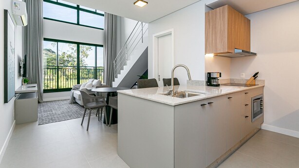 A modern kitchen with a built-in oven, a dining area with a table and chairs, and a staircase leading to a balcony.