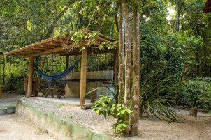Uma pérgola de madeira com uma rede, rodeada por vegetação densa.