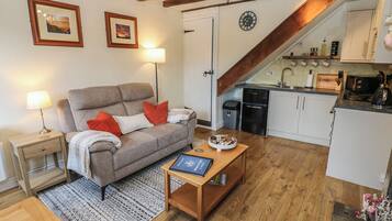 A cozy living room with a sofa, a coffee table, and a kitchen area with a sink and cabinets.