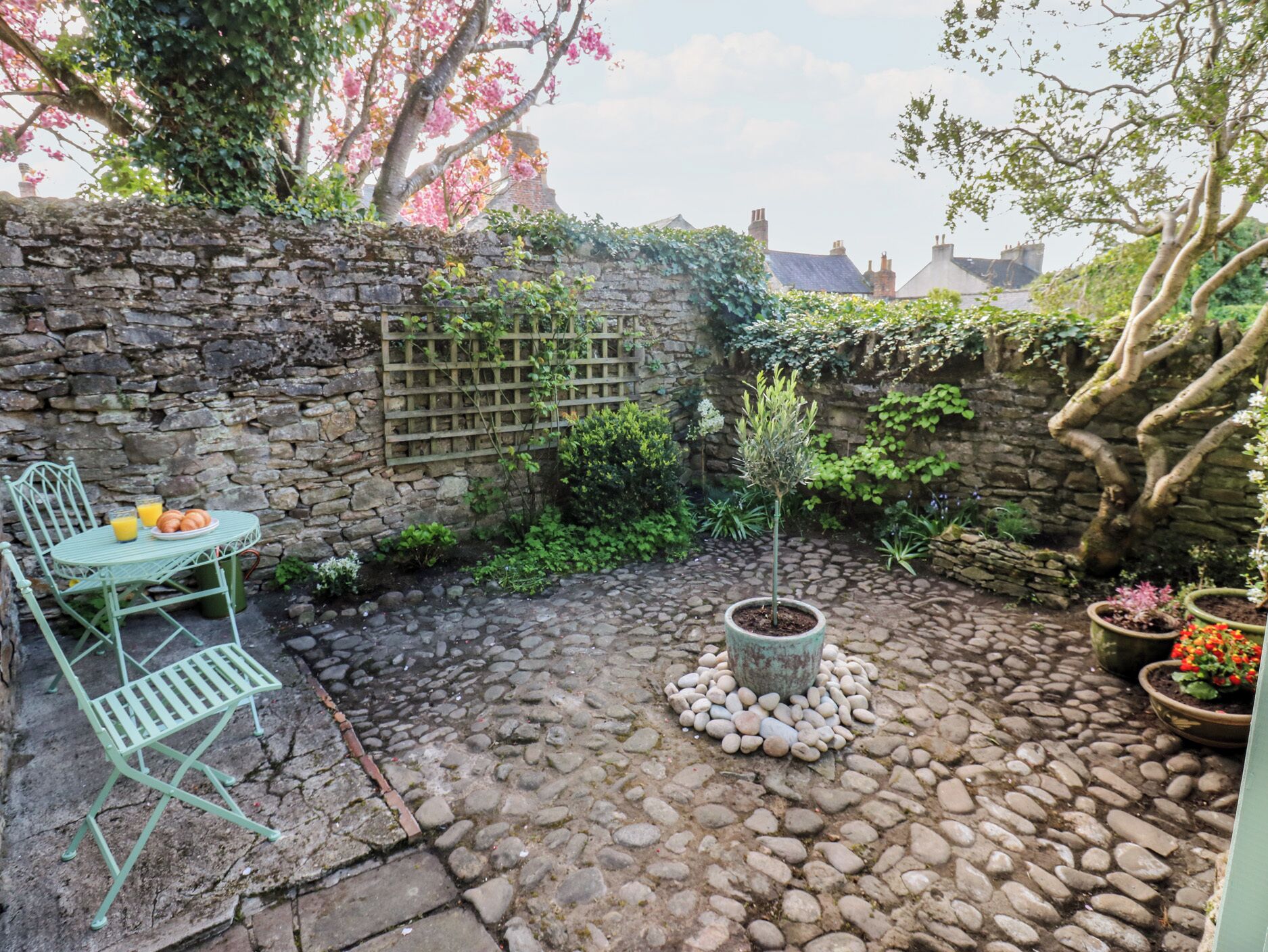 A stone wall, a small tree, and a table with chairs in a courtyard.