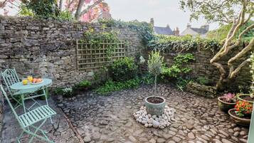 Un muro de piedra, un árbol pequeño y una mesa con sillas en un patio.