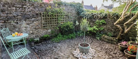 A stone wall, a small tree, and a table with chairs in a courtyard.