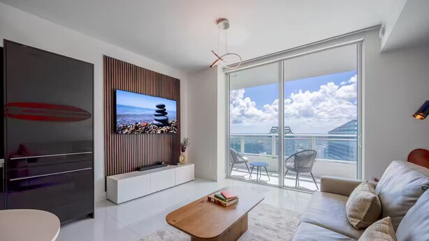 Ein modernes Wohnzimmer mit Flachbildfernseher, einer Holz-Unterhaltungsecke, einer Couch, einem Couchtisch und einem Balkon mit Blick auf die Stadt.